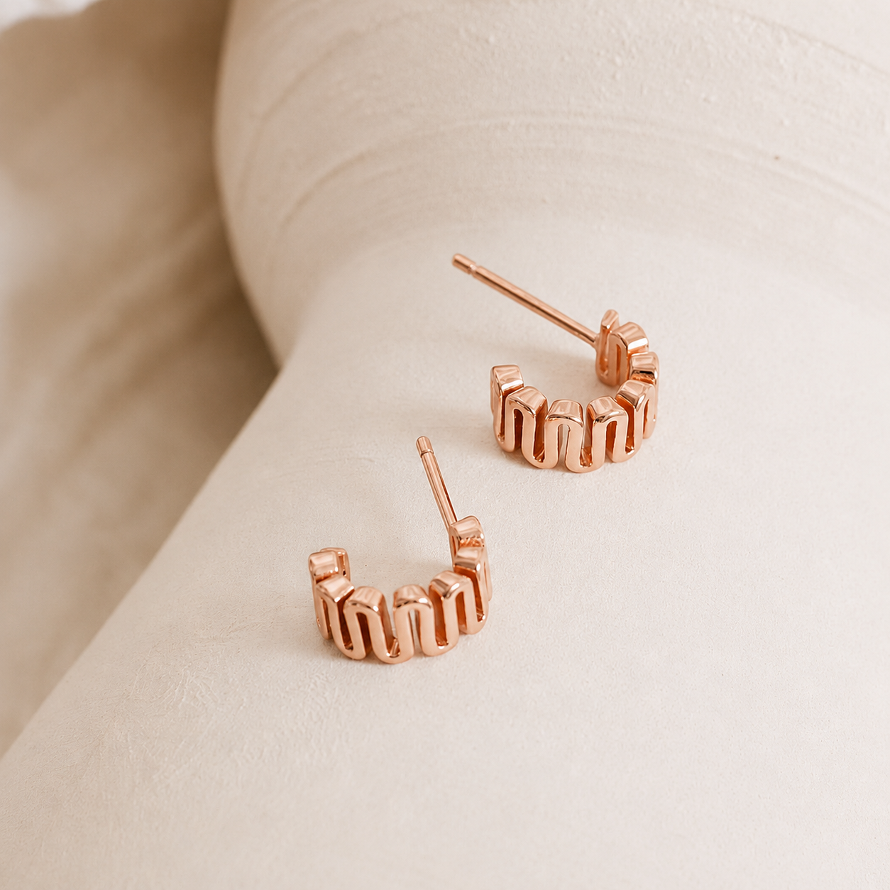 Rose gold hoop earrings on a light beige surface